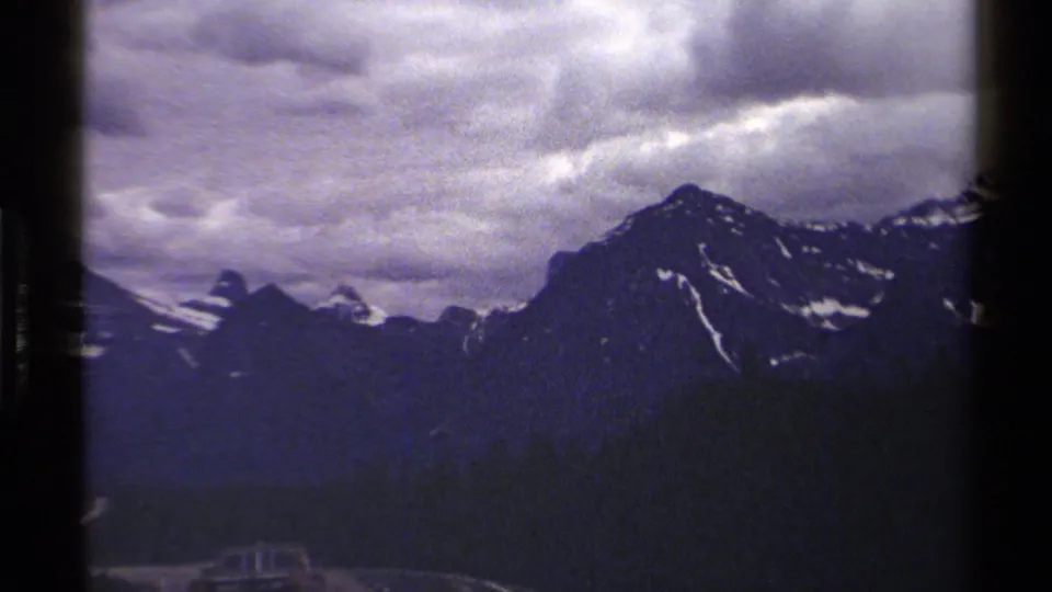 A steady 8mm pan across British Columbia alpine ridges, with snow traces and a cloudy sky.