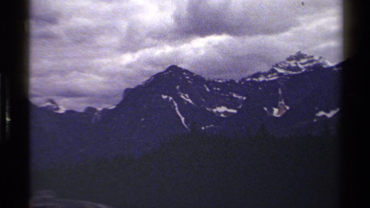British Columbia alpine peaks appear in a grainy 1979 8mm frame, with snow on dark rock faces.