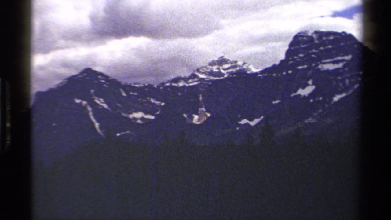 The 1979 8mm pan ends on a wider British Columbia mountain face with snow pockets and cloud cover.