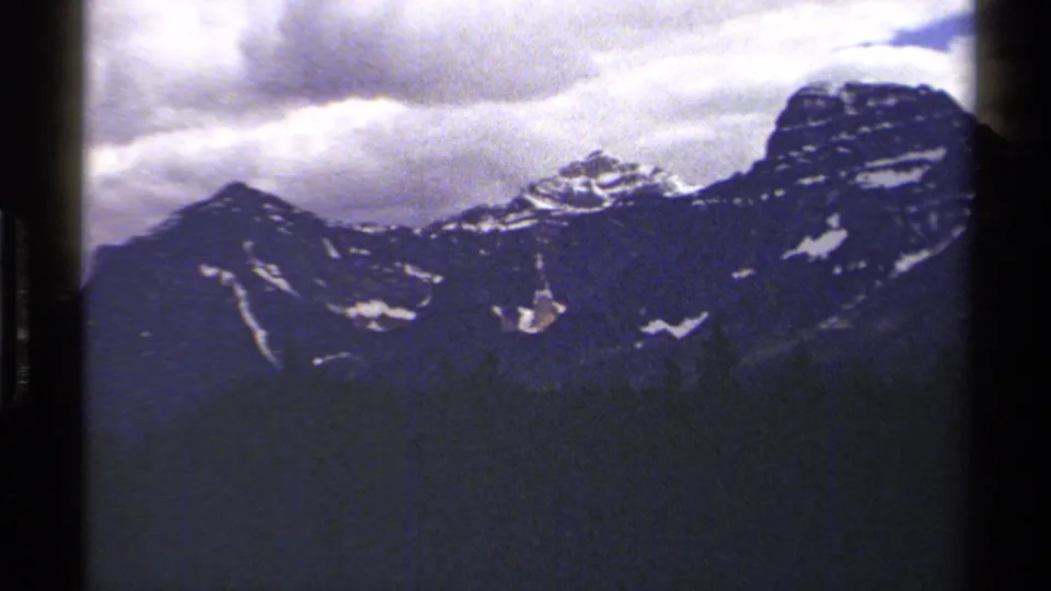 The 1979 8mm pan ends on a wider British Columbia mountain face with snow pockets and cloud cover.