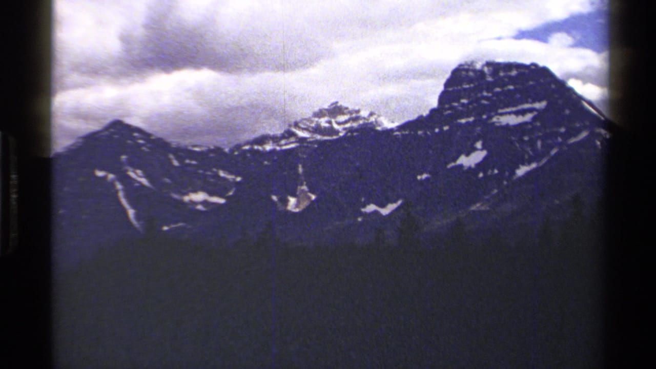 Snow-dusted mountain range beneath thick clouds, framed by dark 8mm film edges.