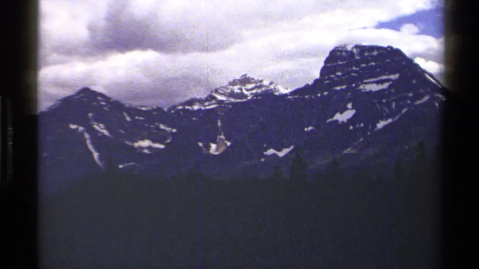 1979 8mm British Columbia travel footage showing distant snow-dusted mountains under a clouded sky, with dark film borders visible.