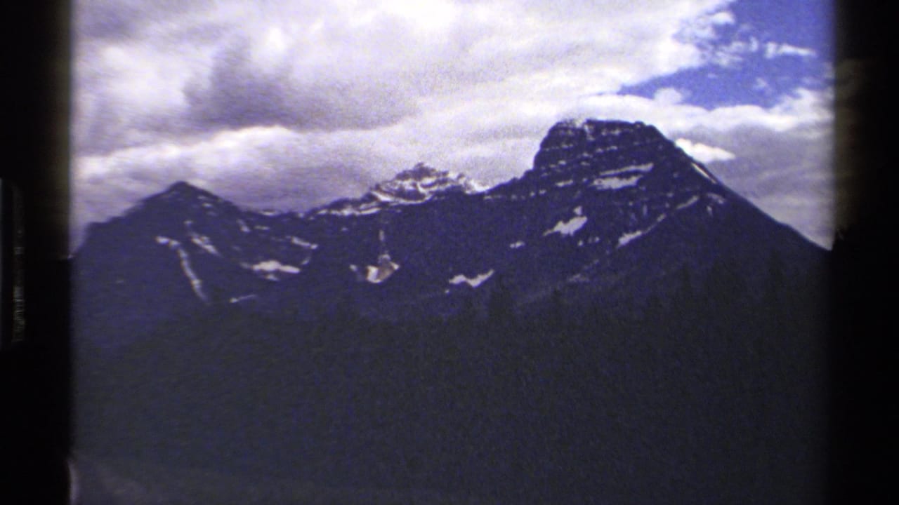 Mountain peaks and cloudy sky with soft grain and dark vertical film edging.