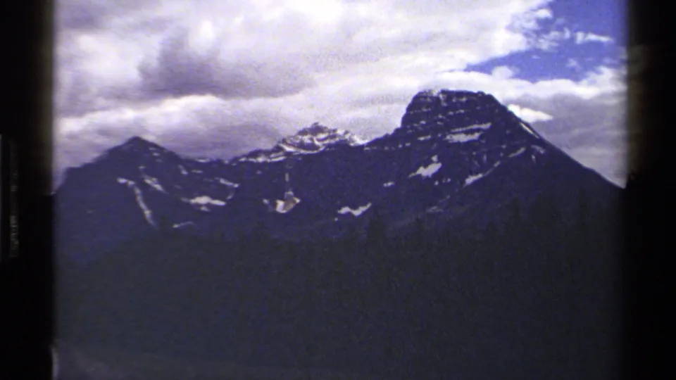 Distant British Columbia mountain peaks appear beneath heavy clouds in soft, grainy 8mm footage from the 1979 home-movie source.