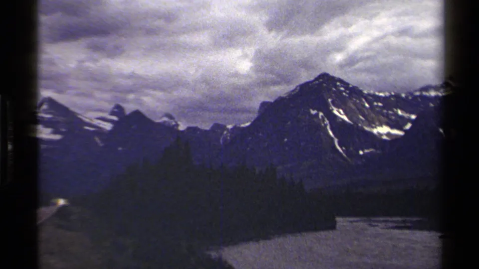 British Columbia mountain scenery on 8mm film, showing forest, a partial highway edge, and a river below the peaks.