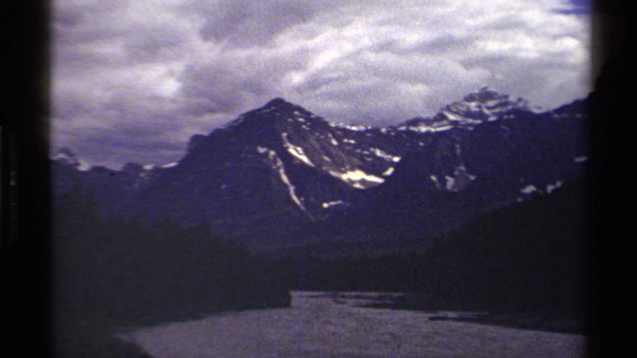 Late-frame 1979 British Columbia landscape with river, evergreen trees, and snow-marked mountains in a soft 8mm scan.