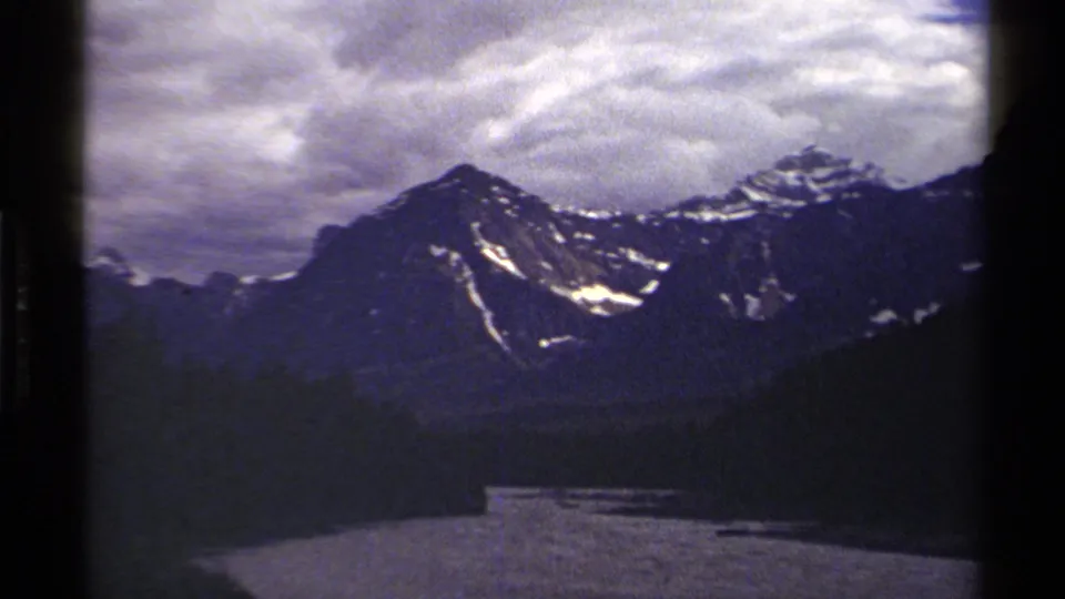 Late-frame 1979 British Columbia landscape with river, evergreen trees, and snow-marked mountains in a soft 8mm scan.