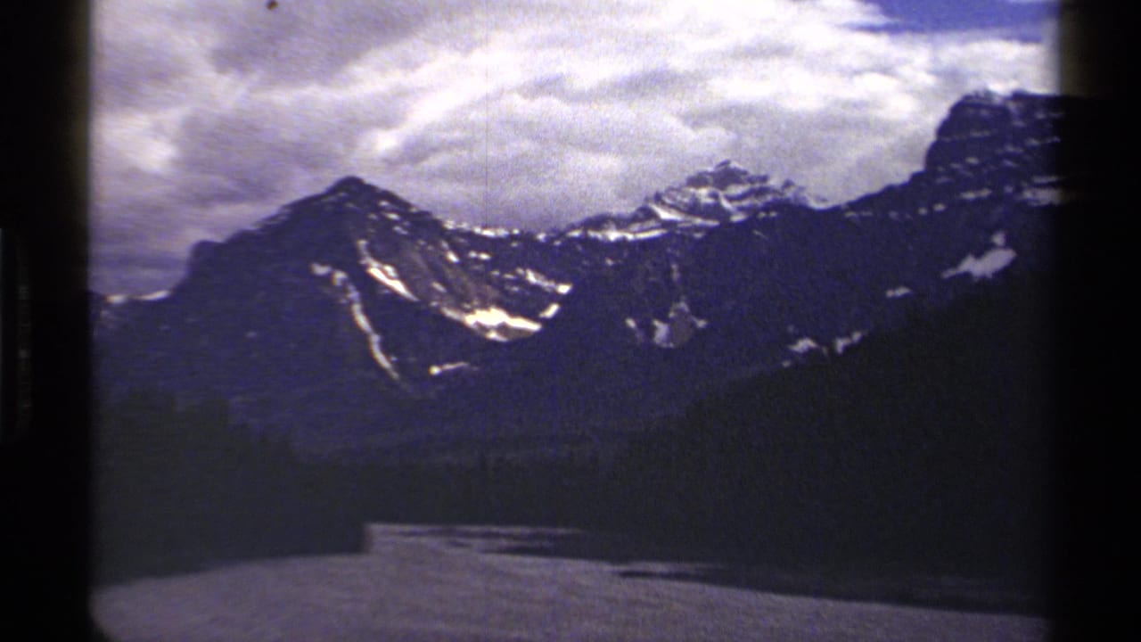 1979 8mm travel footage showing a Canadian mountain range with snow patches, heavy clouds, and dark foreground slopes.