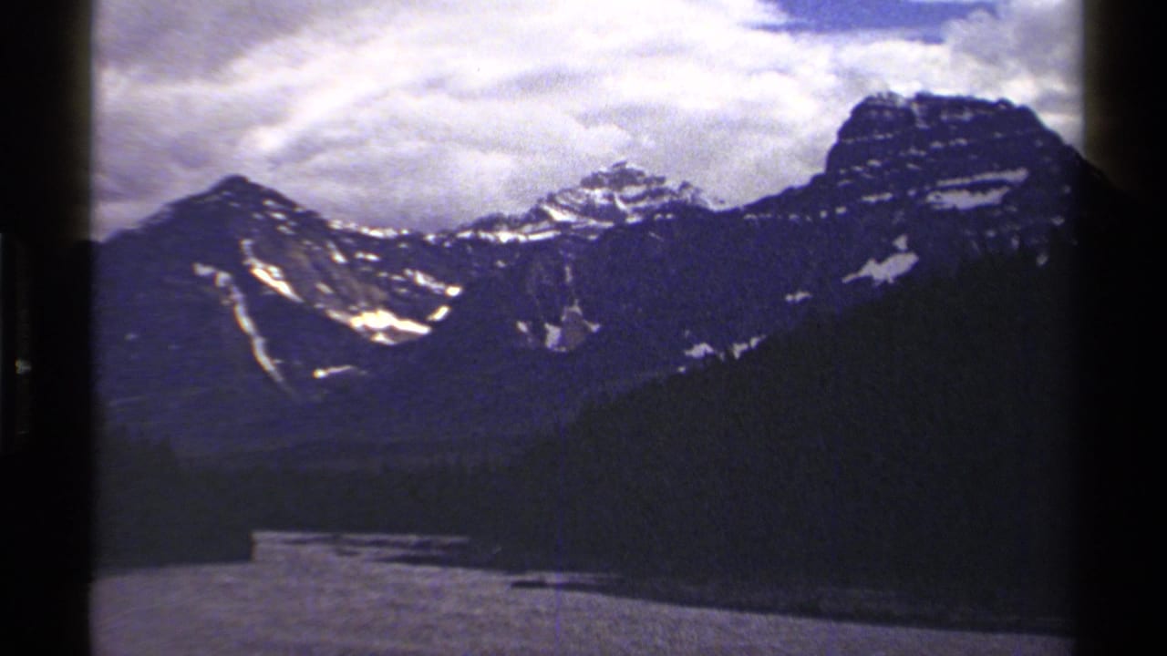 Mountain peaks and dark valley landscape beneath a bright cloudy sky.