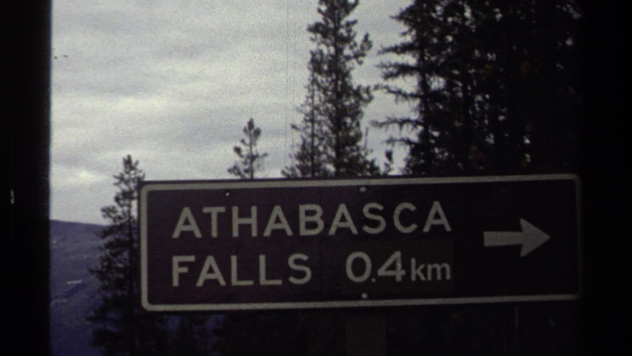 1979 8mm frame of an Athabasca Falls 0.4 km direction sign against trees, based on clip metadata.