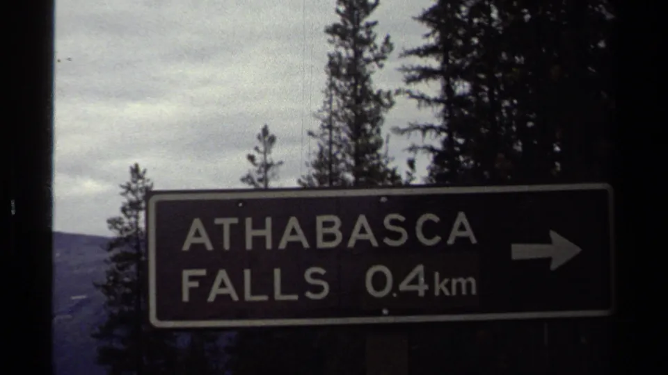 1979 8mm frame of an Athabasca Falls 0.4 km direction sign against trees, based on clip metadata.