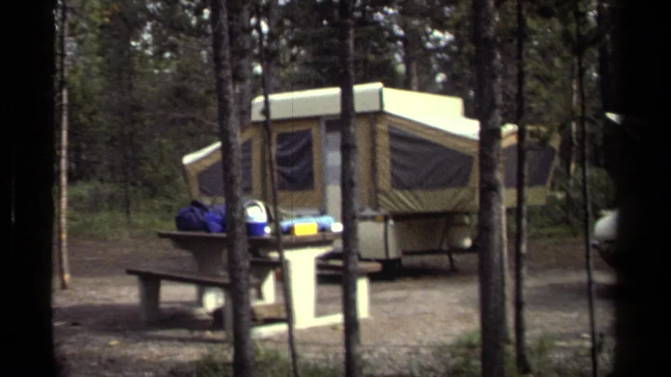 Wooded 1979 campsite frame with pop-up camper, picnic table, campsite post, and partial car at the edge.
