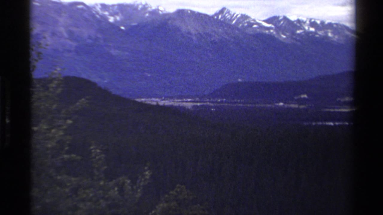 Distant snow-capped mountains beyond dark forested hills and a valley.