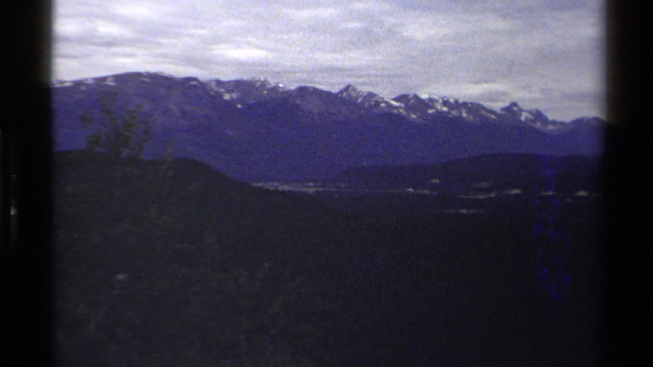 1979 British Columbia 8mm frame of snow-capped mountains across wooded hills, with hazy exposure and visible film edges.