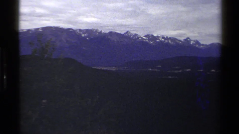 1979 British Columbia 8mm frame of snow-capped mountains across wooded hills, with hazy exposure and visible film edges.