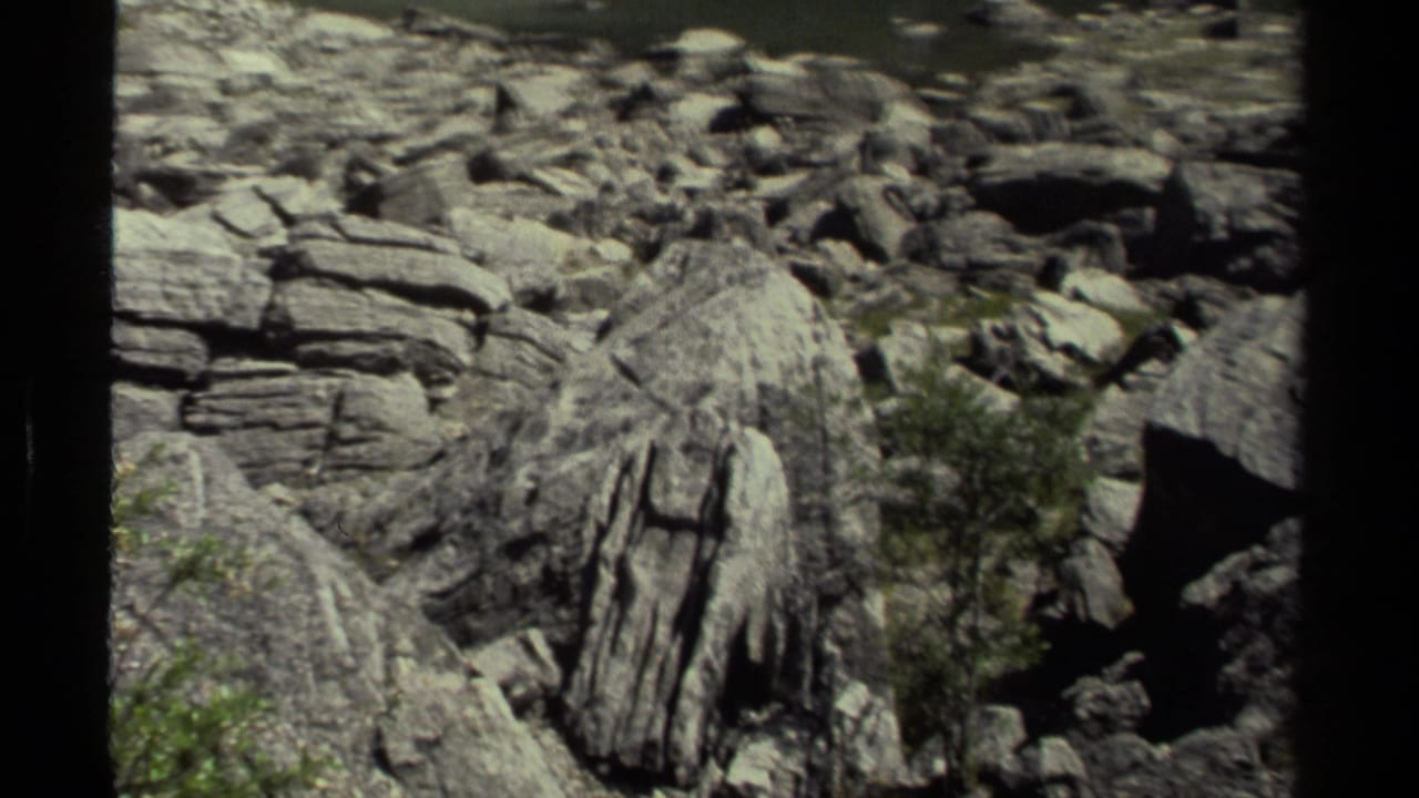 Close view of pale layered rocks and boulders with shrubs in a rugged landscape.