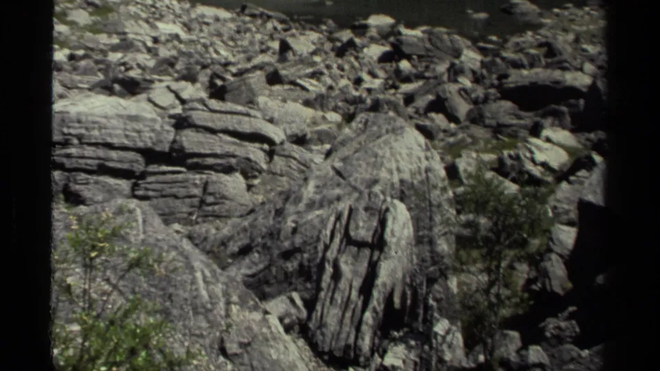 1979 8mm British Columbia footage continuing across a boulder field with layered rock faces, brush, and visible film-frame borders.