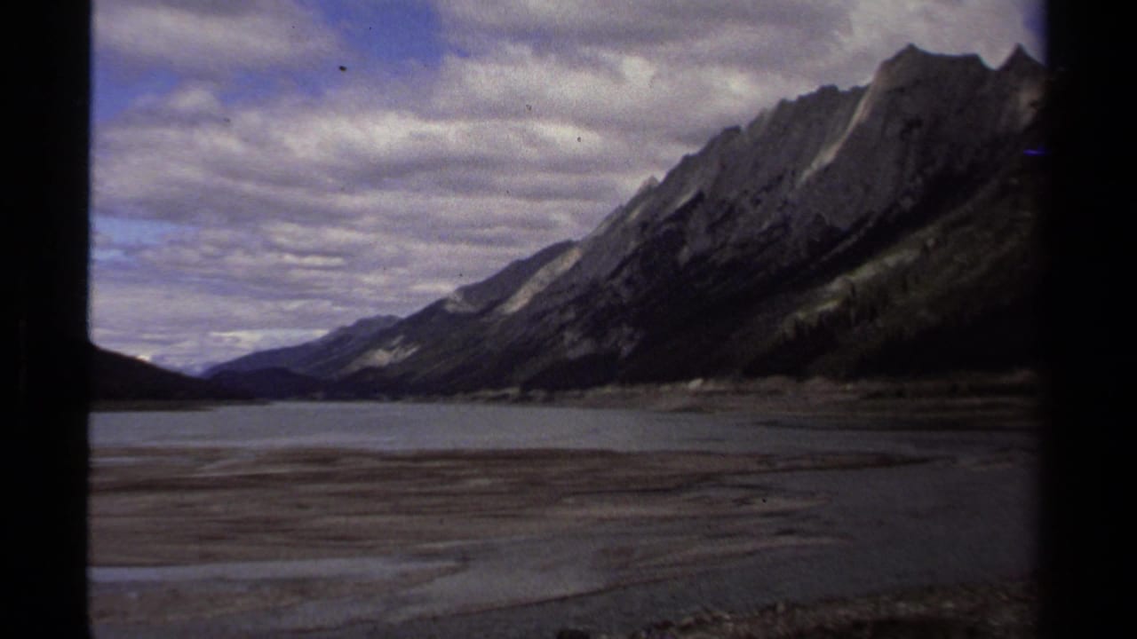 Rugged mountain ridge above broad water and gravel flats beneath clouds.