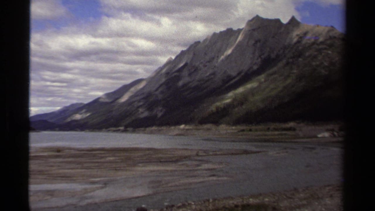 1979 British Columbia 8mm frame with a rocky mountain slope, calm water, gravel flats, and soft home-movie color.