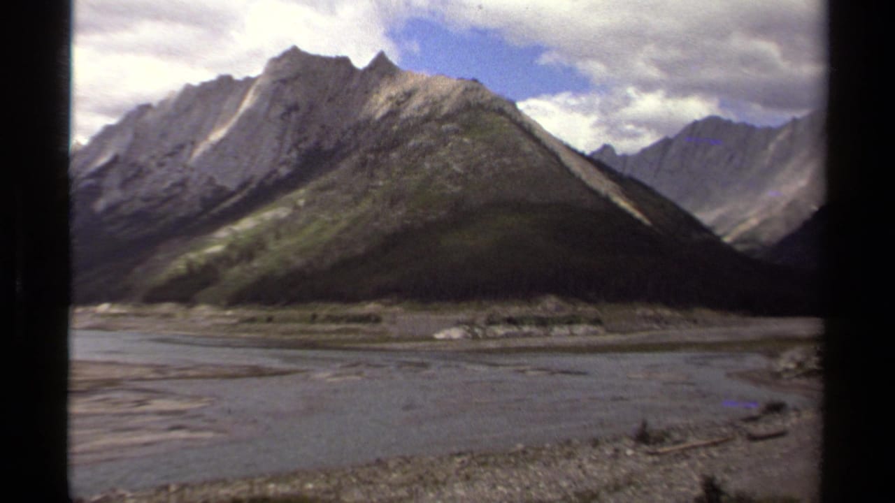 Rocky mountain ridge with water in the foreground and clouds overhead.