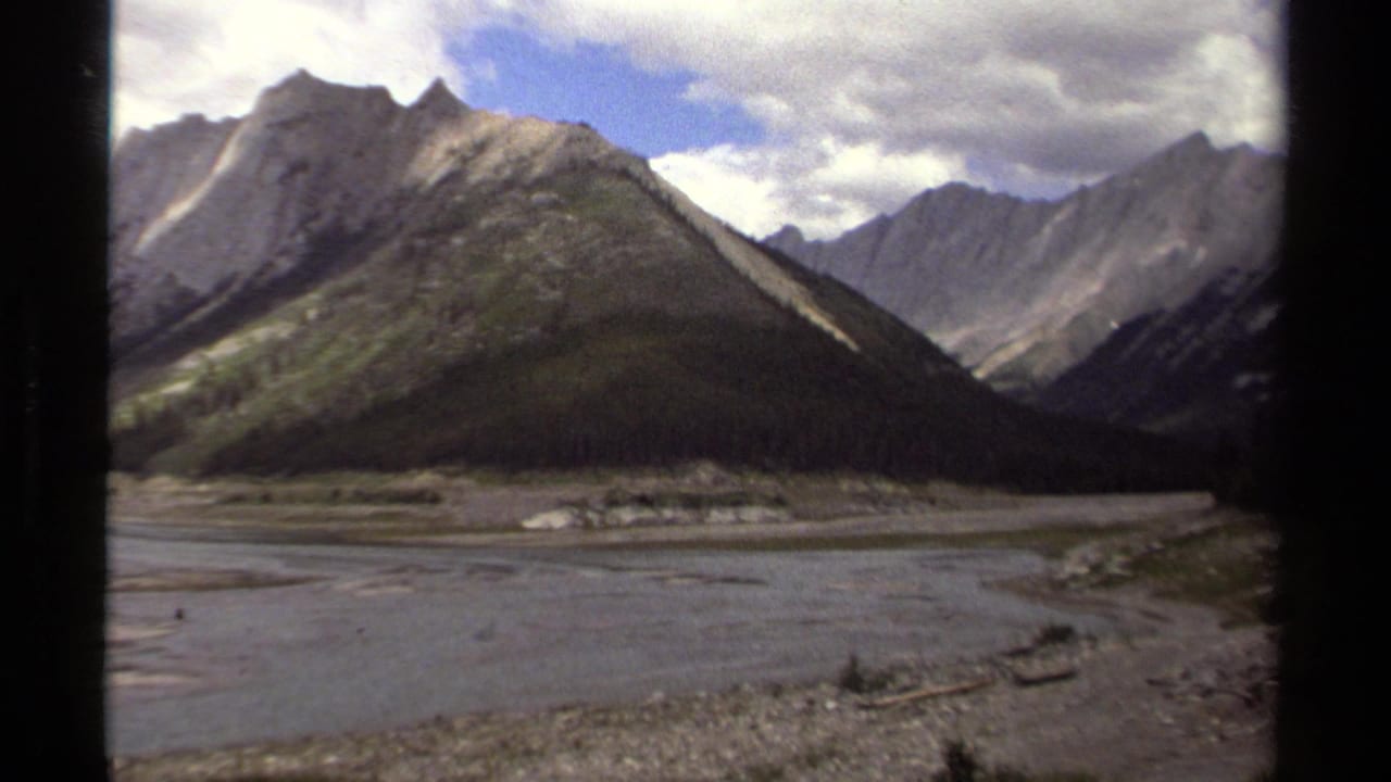 1979 British Columbia 8mm frame looking across braided water or shoreline toward a rugged mountain valley.