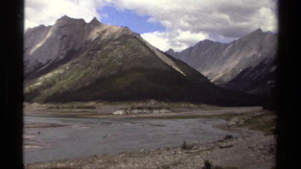 1979 British Columbia 8mm frame looking across braided water or shoreline toward a rugged mountain valley.