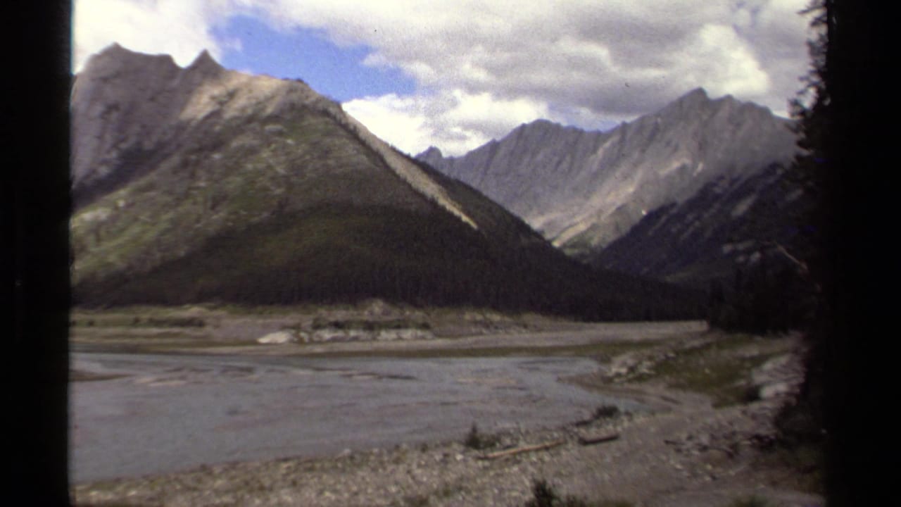 1979 8mm British Columbia view of a broad riverbed running through a rugged mountain valley under broken clouds.