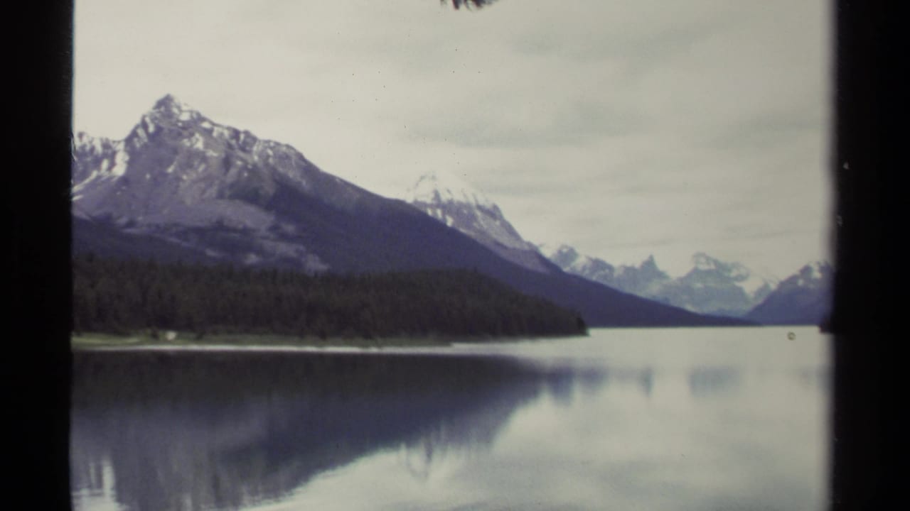 1979 8mm British Columbia view of a dark mountain peak over evergreen shoreline and glassy lake water with soft reflections.