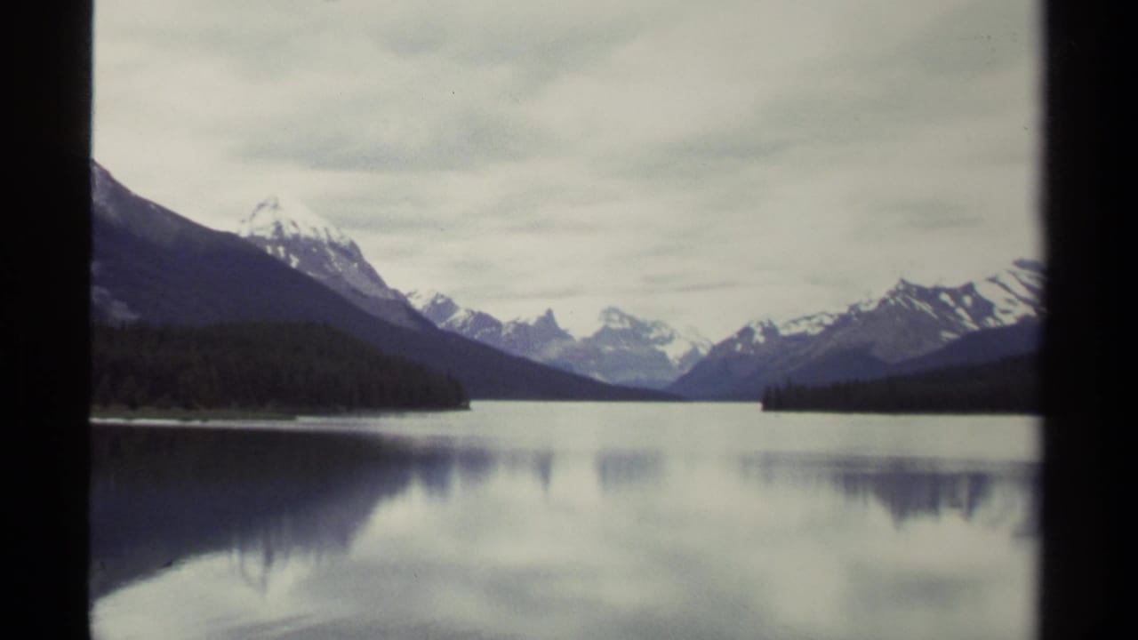 8mm frame from British Columbia in 1979 showing a quiet lake, mountain range, forested banks, and cloudy sky within visible film borders.