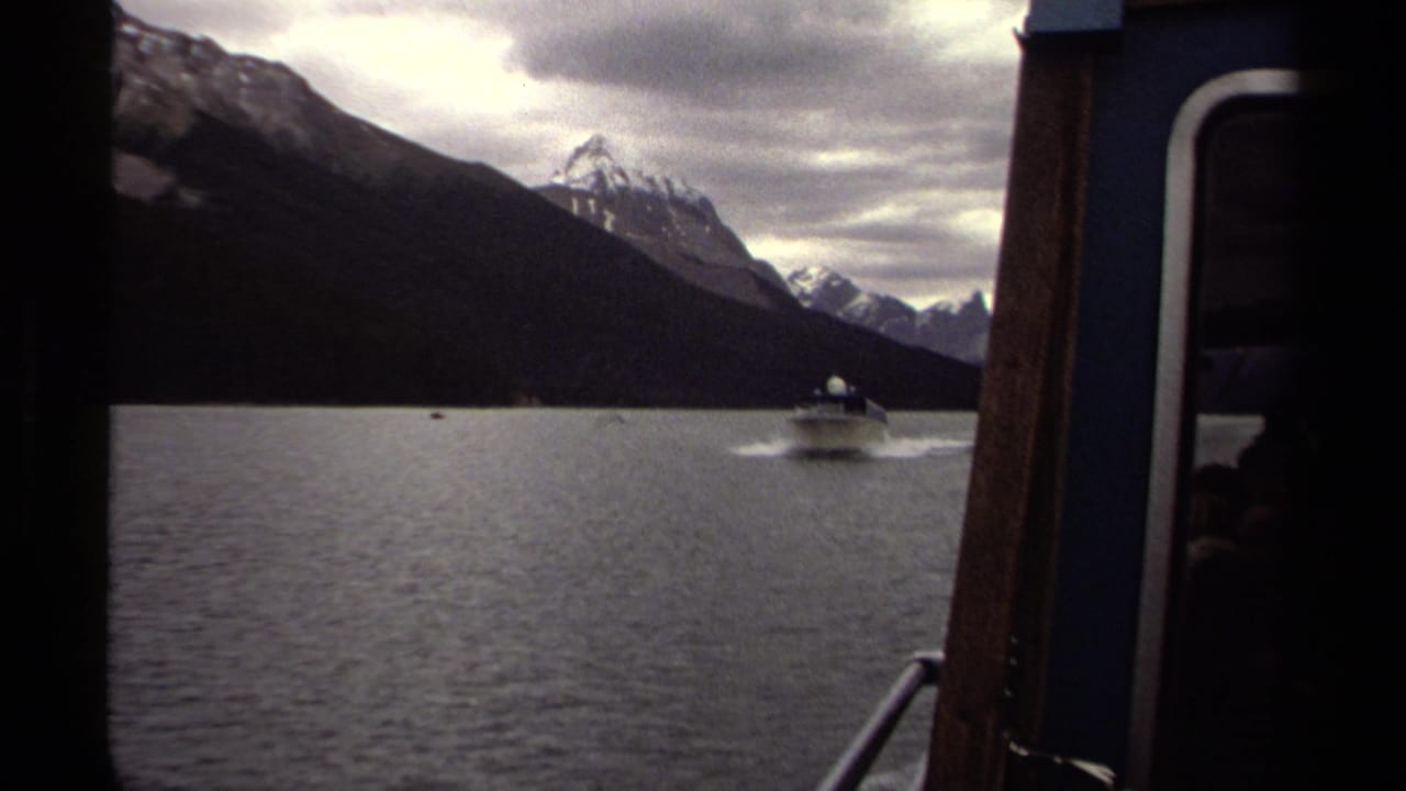 Small motorboat travels across open water with mountains and forested shore behind it.
