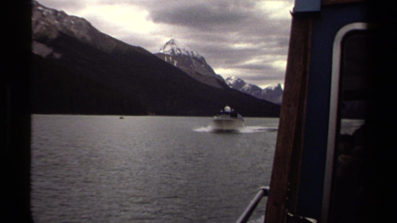 8mm British Columbia lake footage showing a motorboat and wake, with snow peaks and the side of the filming boat in frame.