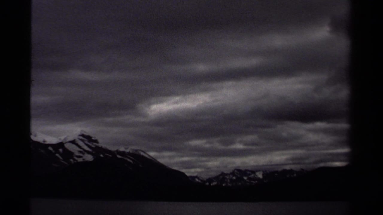 British Columbia mountain silhouettes and lake water appear in a dark, grainy 8mm frame from a 1979 boat trip.