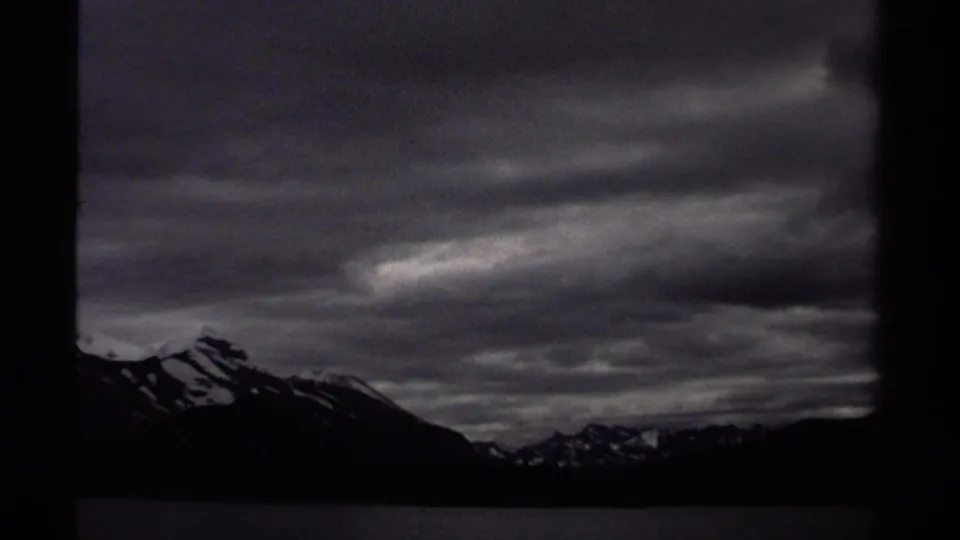 British Columbia mountain silhouettes and lake water appear in a dark, grainy 8mm frame from a 1979 boat trip.