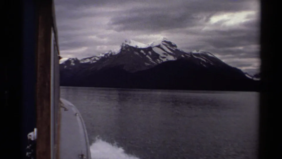 From a moving boat, the 1979 8mm footage looks across a British Columbia lake toward snow-dusted mountains and cloudy sky.