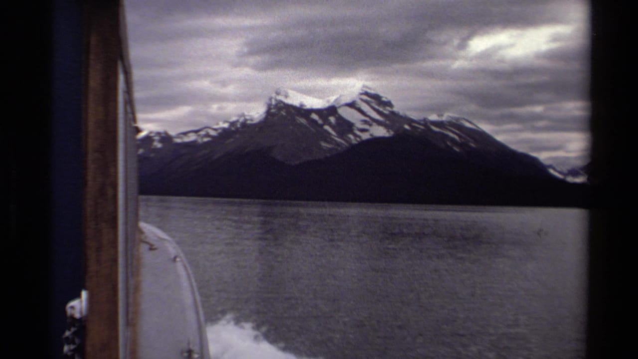 Lake and mountain range seen from a boat with cloudy sky overhead.