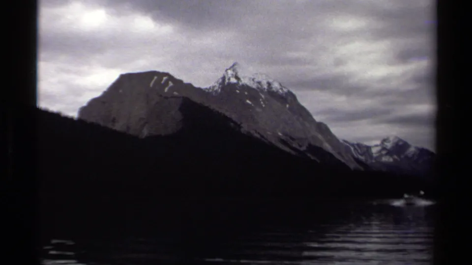 A darker 8mm frame shows lake water, silhouetted shoreline, rugged mountains, and bright cloud breaks in British Columbia.