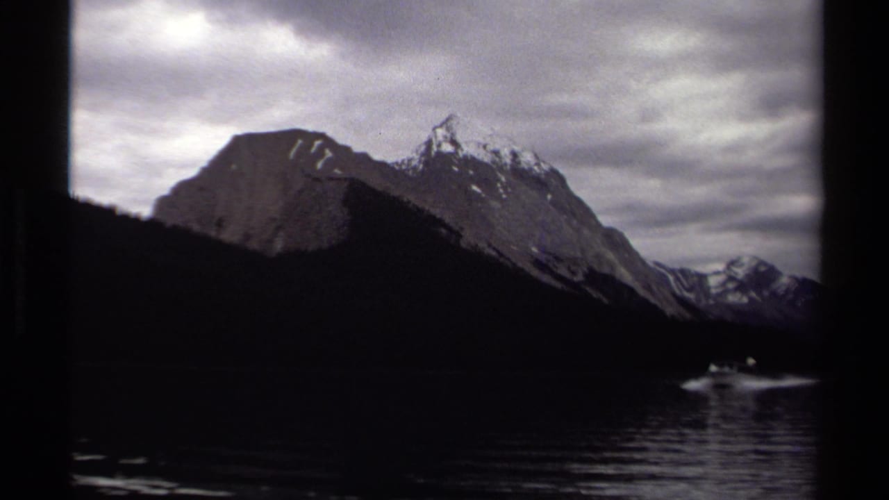 1979 8mm view from a boat on a British Columbia glacial lake, with dark water, mountain ridges, and heavy cloud cover.