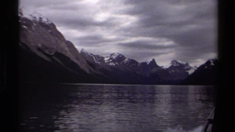 Muted 8mm view of a British Columbia glacial lake bordered by snow-capped mountains, with boat structure at the frame edge.