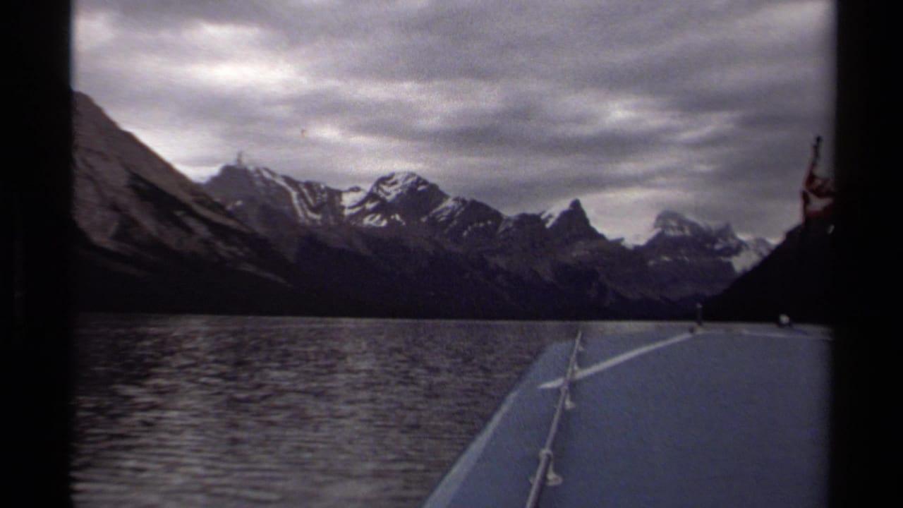 1979 British Columbia home-movie frame from a moving boat, looking across lake water to rugged snowy peaks and cloudy sky.