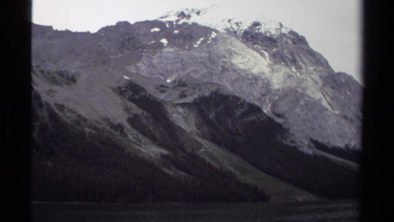 1979 British Columbia home-movie view of a snow-marked mountain rising above evergreen forest and a calm lake.