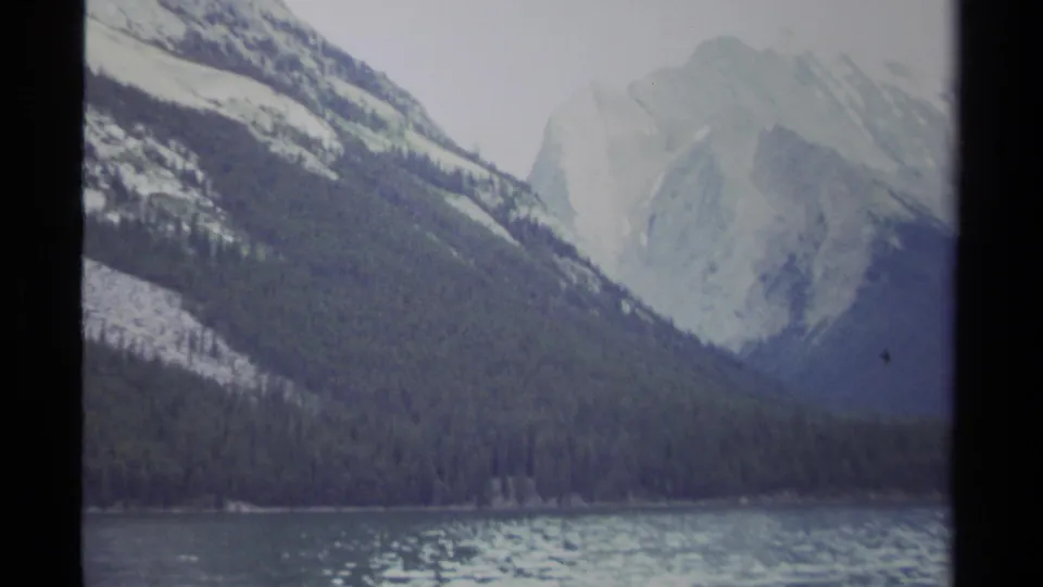 1979 British Columbia 8mm landscape with evergreen-covered slopes, pale rocky mountains, and rippled lake water.