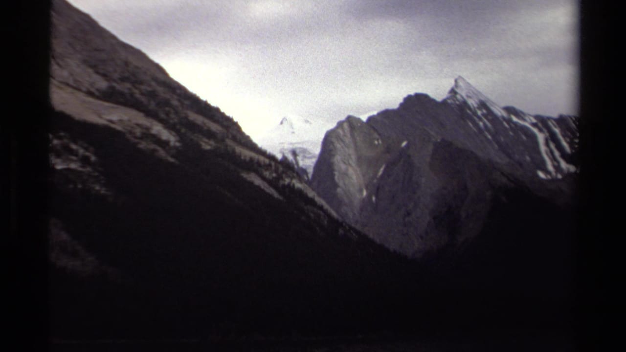 Dark mountain valley with snow peaks in the distance and black film borders.