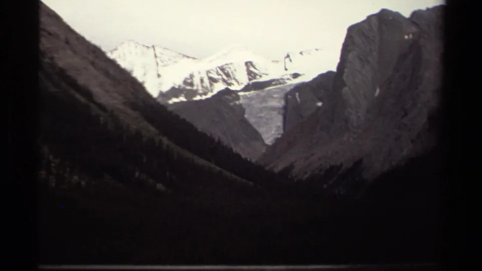 1979 British Columbia 8mm frame with snow peaks, a light snowfield, and dark V-shaped valley slopes in a handheld home-movie view.