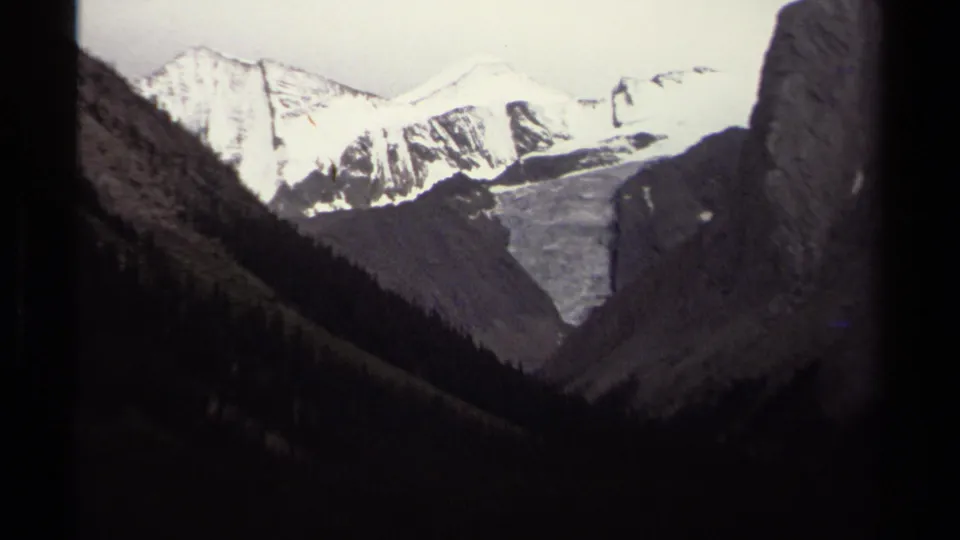 1979 British Columbia 8mm frame showing distant alpine snow peaks and a pale glacier-like field between dark ridges.