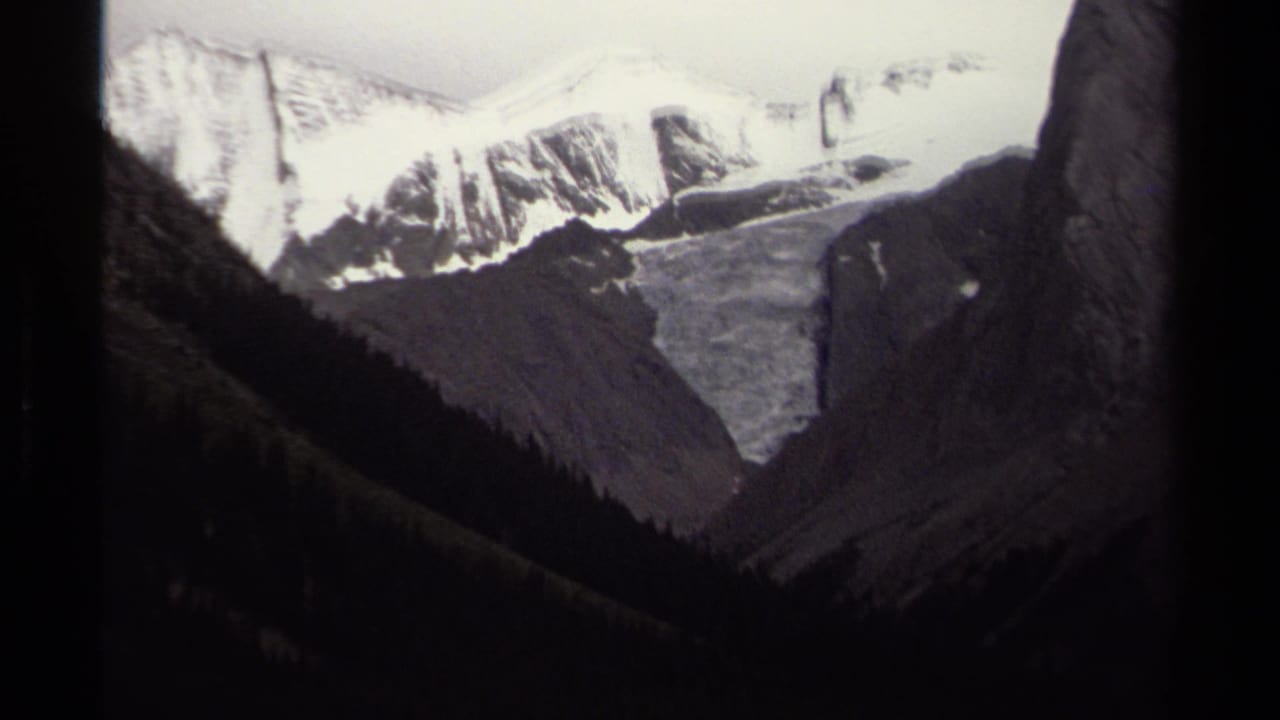 Snow-capped mountain ridge above dark forested slopes and a glacier valley.