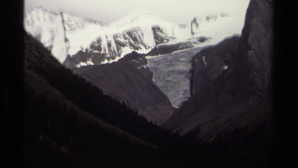 1979 British Columbia 8mm frame showing snow-capped peaks, dark wooded slopes, and a glacier set back in a mountain valley.