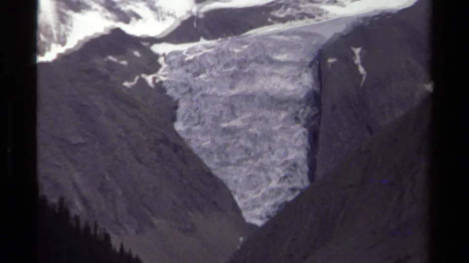 1979 British Columbia 8mm frame showing the glacier enlarged between steep gray slopes, with snow-covered peaks partly cropped above.