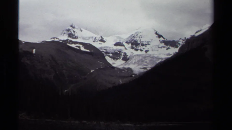 1979 8mm shot of snow-covered British Columbia peaks and glacier ice rising above a shadowed forest valley.