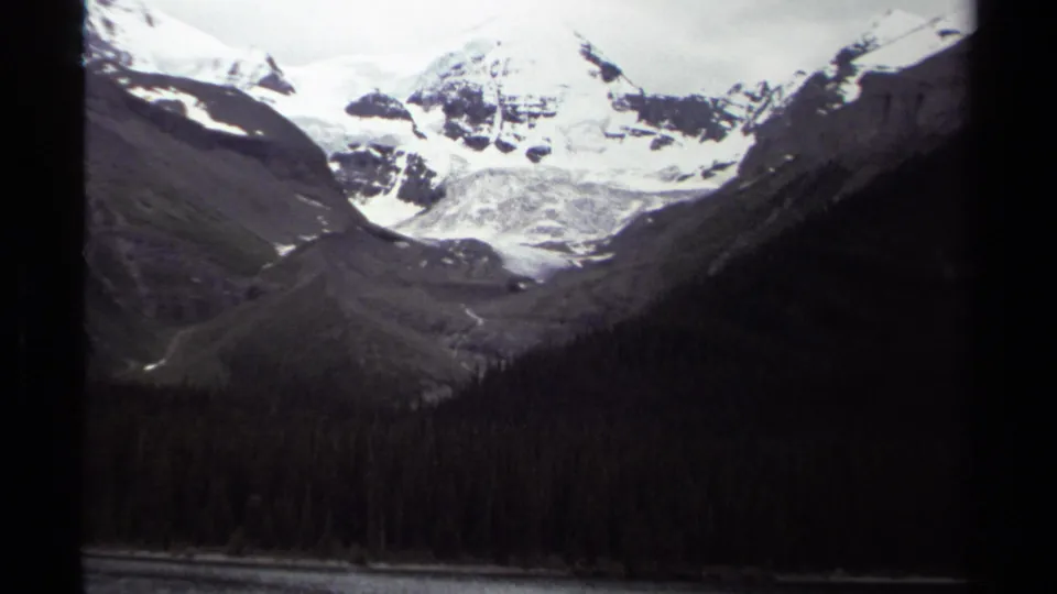 1979 British Columbia 8mm frame showing snowy ridges and a glacier-like mass over a dark evergreen valley.