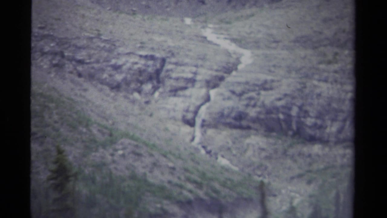 Rocky mountain slope with a narrow pale stream running through sparse greenery.